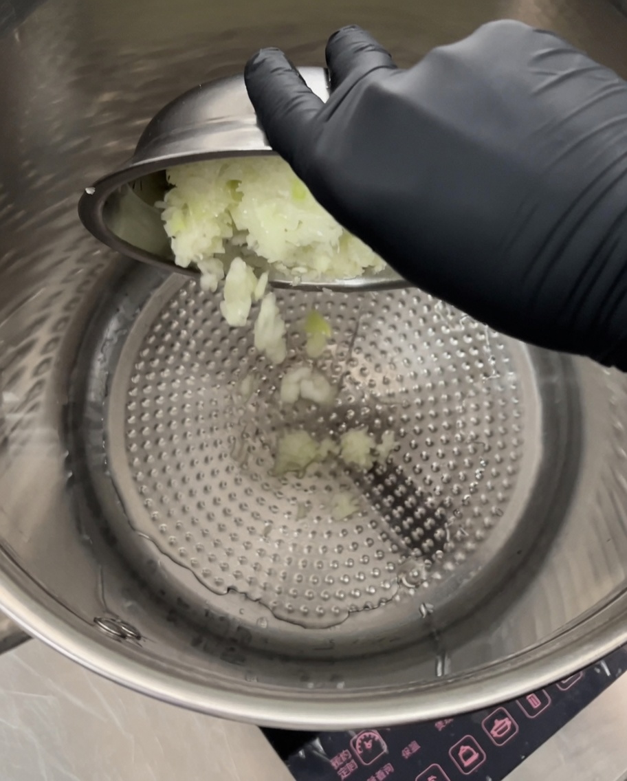 Cebollas finamente picadas siendo revueltas en una olla grande de acero inoxidable a fuego medio.