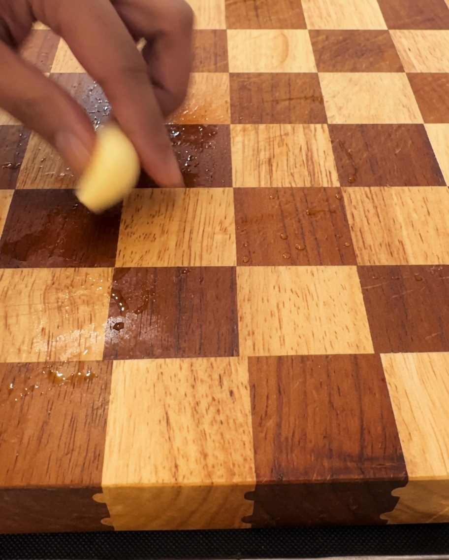 Dientes de ajo siendo finamente picados sobre una tabla de cortar de madera con un cuchillo grande.