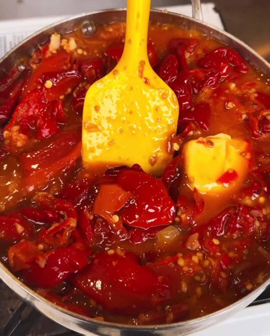 La salsa de chile hirviendo a fuego lento en una sartén mientras se añade una salsa oscura y espesa, creando un acabado rico y brillante.