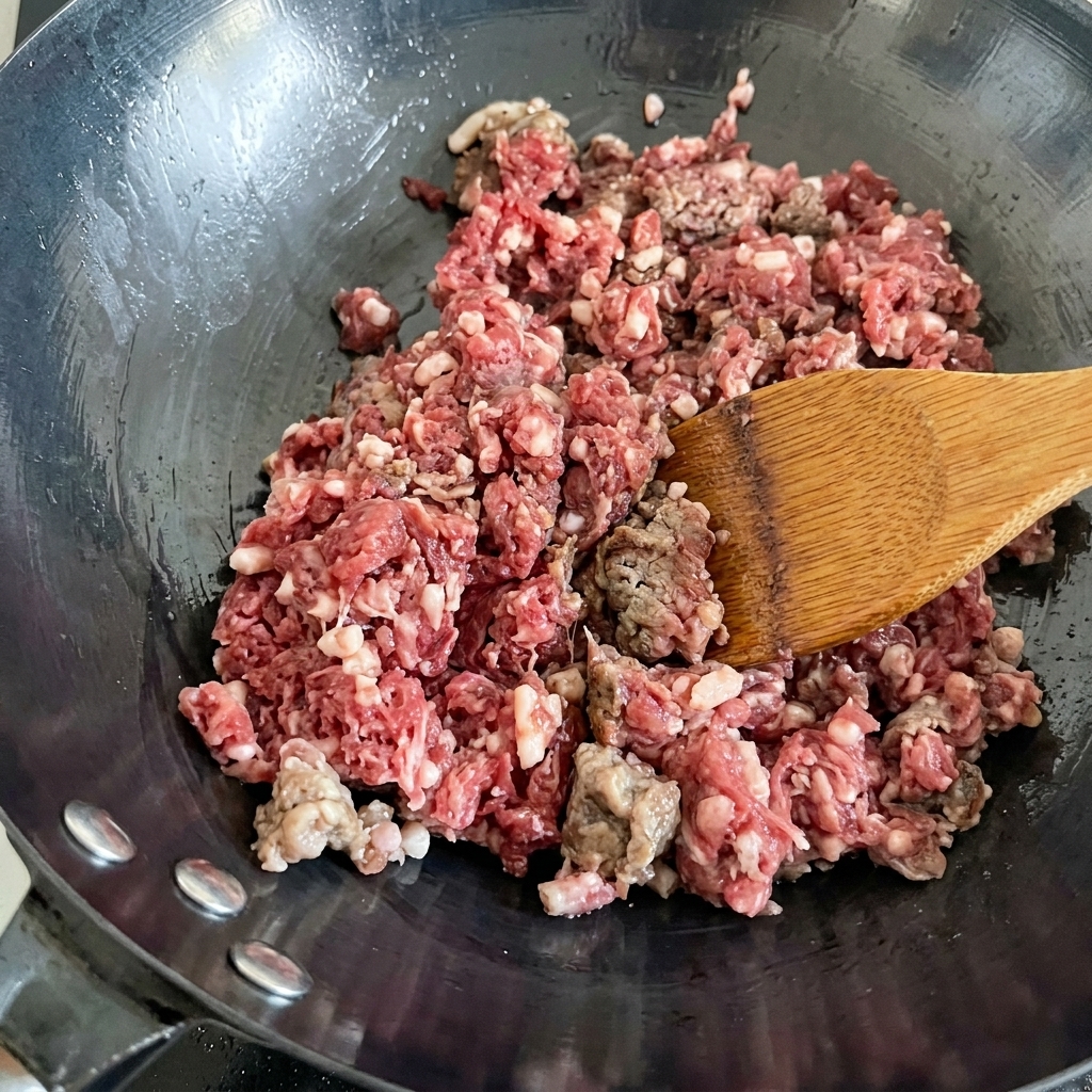 Carne molida fresca siendo salteada en un wok caliente, cambiando de color de rojo a marrón.