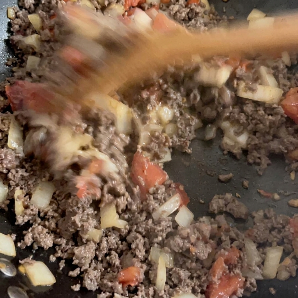 Carne molida dorada y vegetales picados salteados siendo mezclados en un wok.