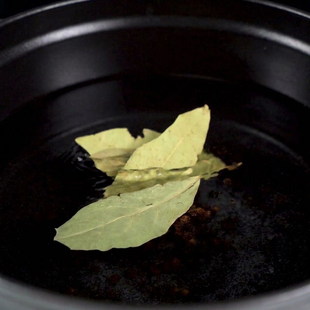 Un bogavante crudo siendo colocado en una olla con agua hirviendo aromática con granos de pimienta y hojas de laurel visibles.