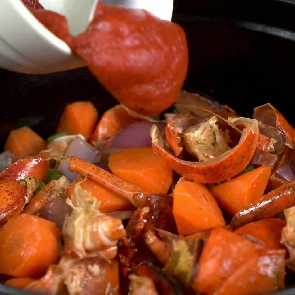 Pasta de tomate siendo removida en la olla de verduras y cáscaras de bogavante.