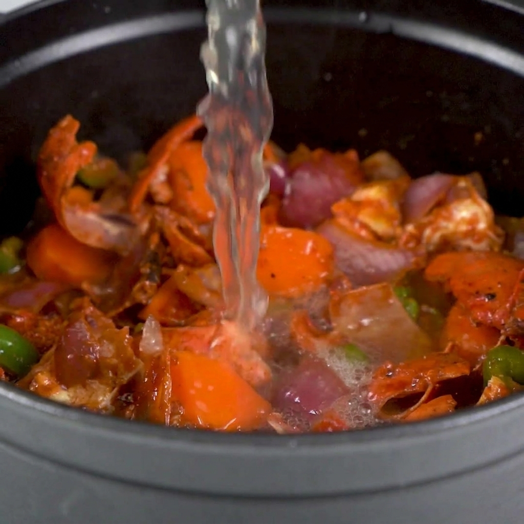 Caldo siendo vertido sobre las cáscaras de bogavante y verduras salteadas en una olla grande.