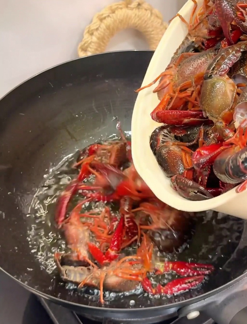 Añadiendo cangrejos a un wok caliente con aceite para freírlos.