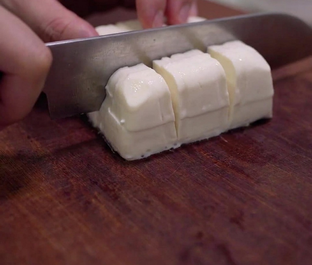 Un bloque de tofu sedoso cortado cuidadosamente en cubos pequeños sobre una tabla de cortar de madera.