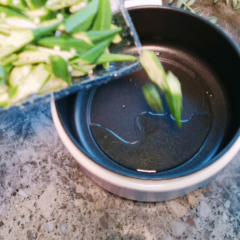 Trozos de okra siendo salteados en una olla caliente con un poco de aceite.