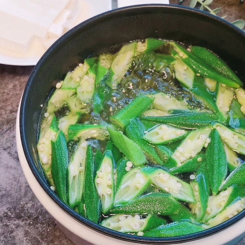 Cubos de tofu suave siendo añadidos a una olla hirviendo de okra y agua.
