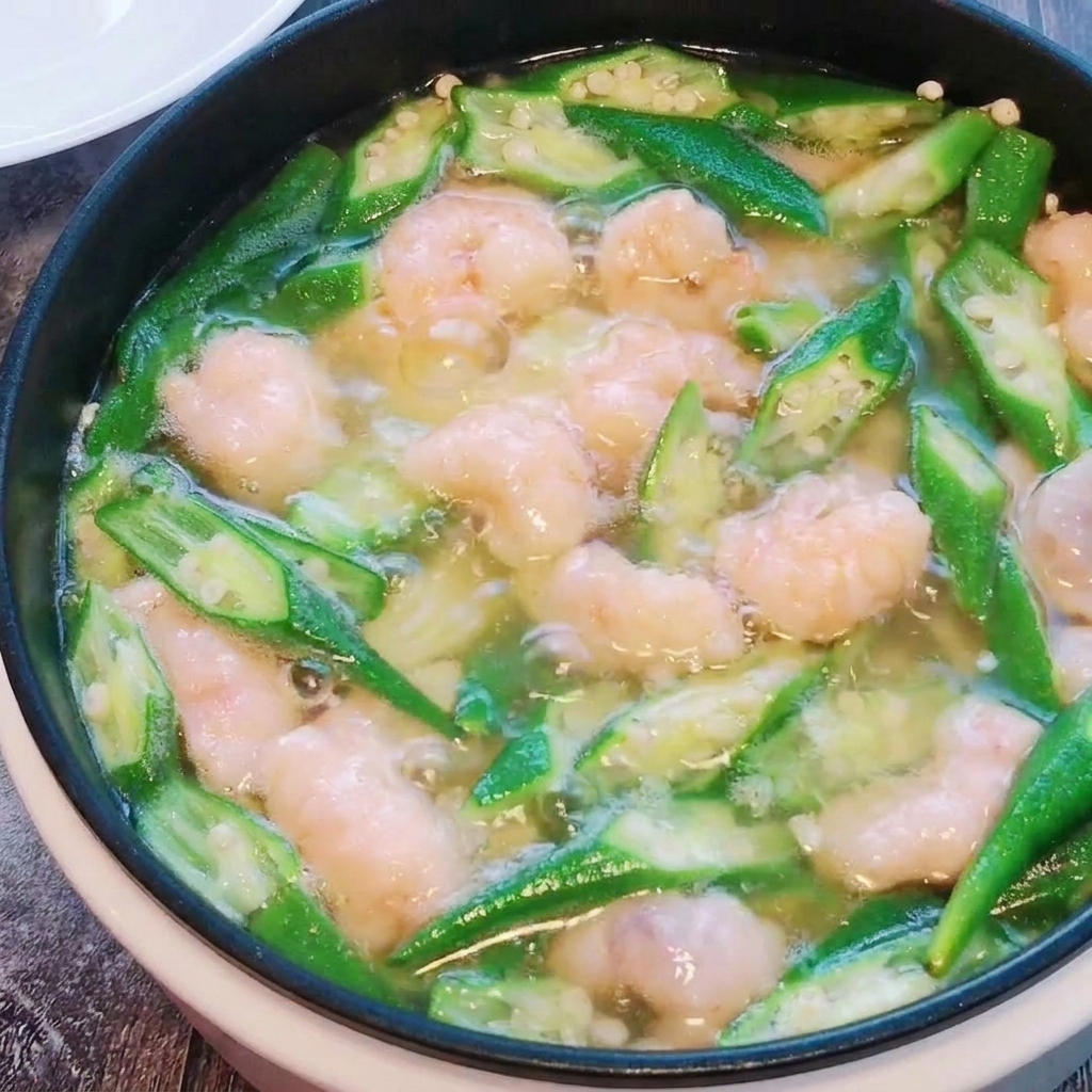 Las bolitas de pasta de camarón siendo removidas suavemente en la sopa de okra y tofu mientras se cocinan.