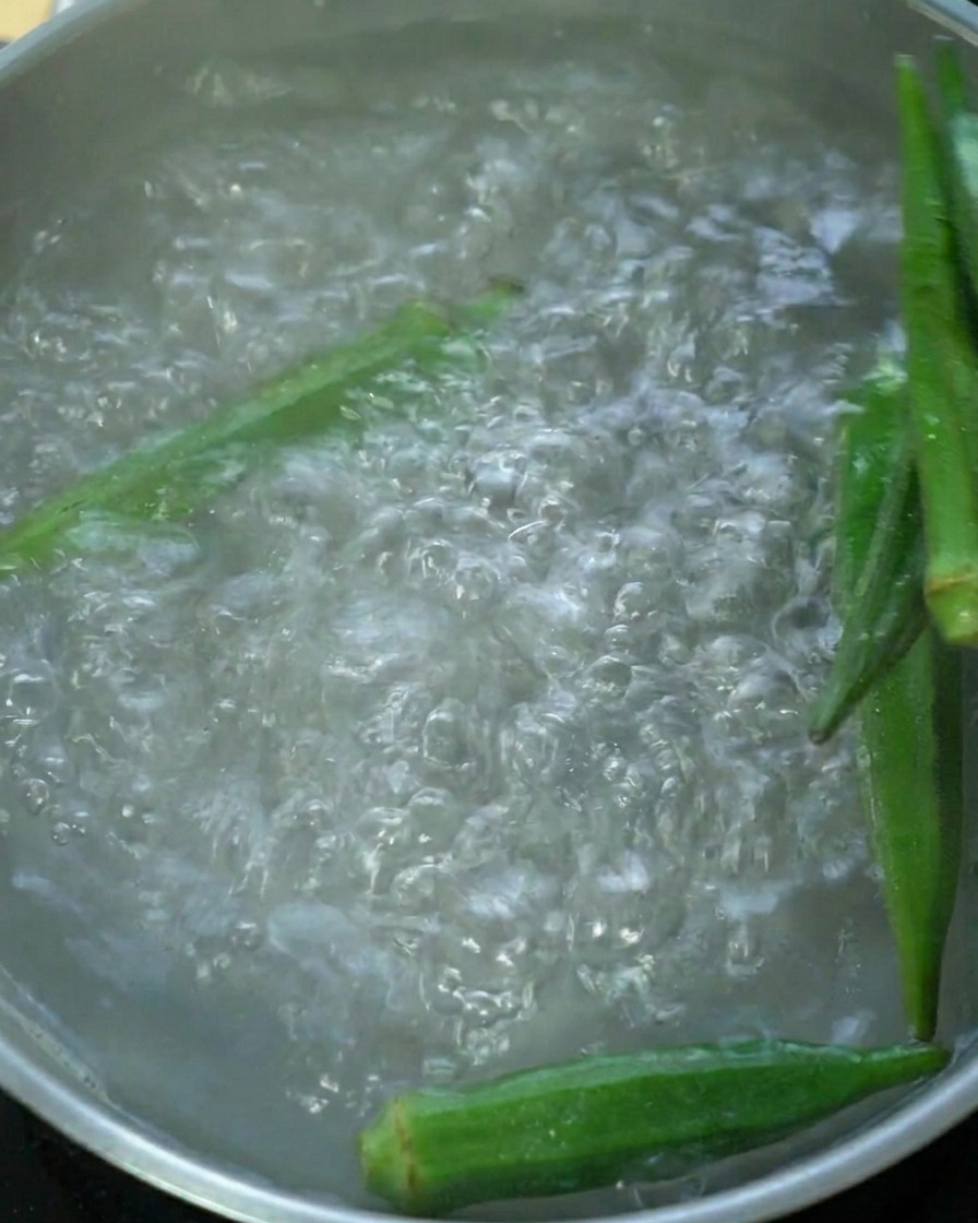 Vainas de okra verde fresca hirviendo en una olla con agua.