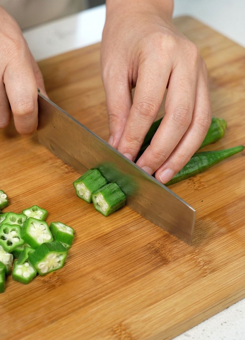 Okra siendo cortada en rodajas sobre una tabla de madera.