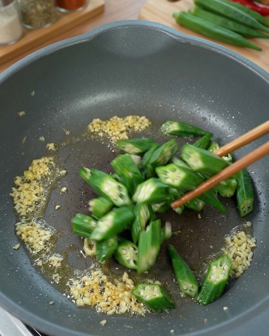 Okra en rodajas siendo salteada en una sartén con jengibre y aceite.