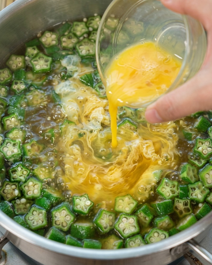 Huevo batido siendo vertido en la sopa de okra hirviendo para crear cintas.