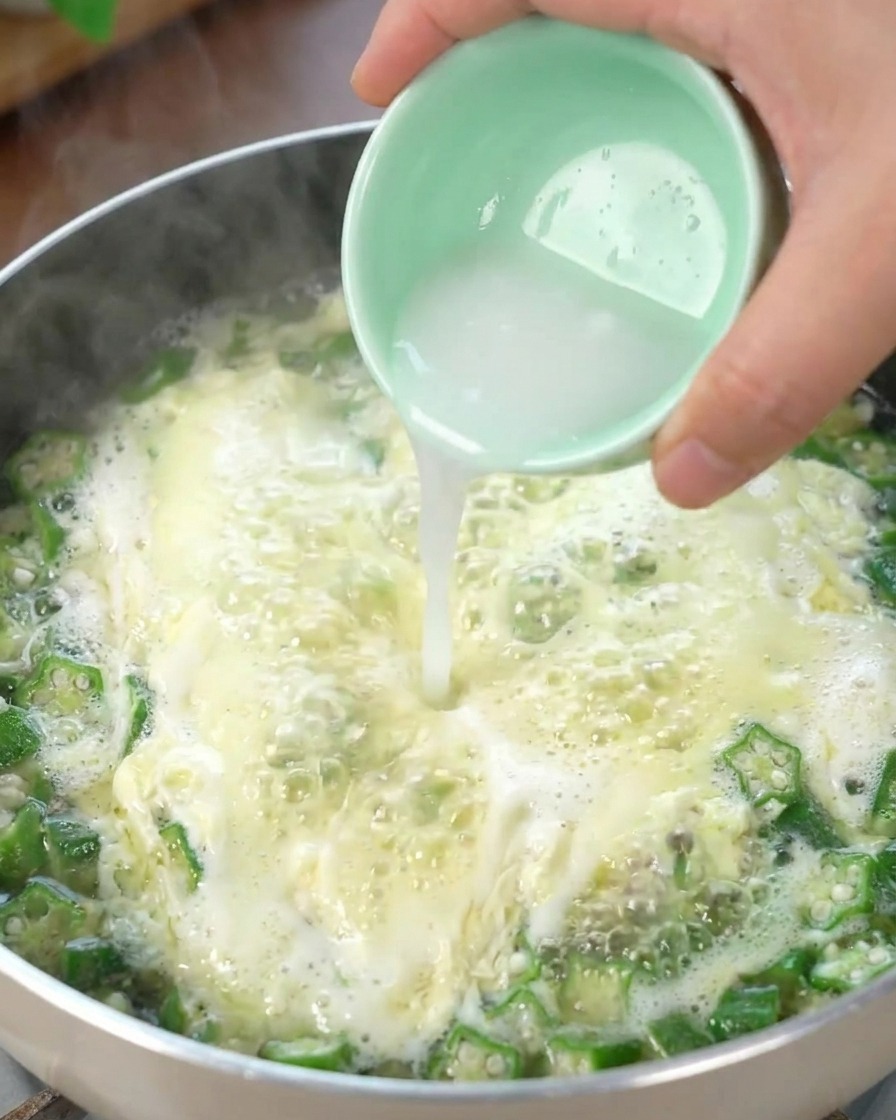 Agua con almidón siendo vertida en la Sopa de Huevo con Okra burbujeante, espesando el caldo.