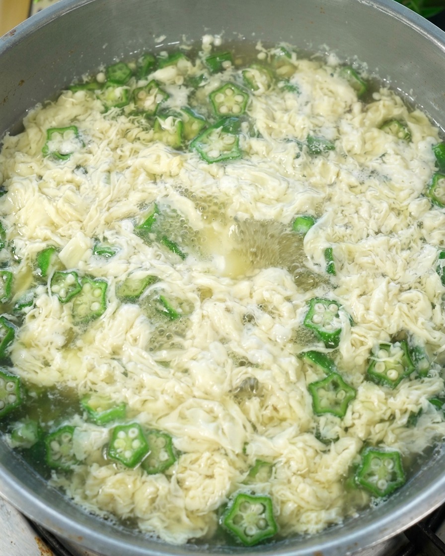 Sopa de Huevo con Okra en la olla con sal siendo añadida, lista para servir.