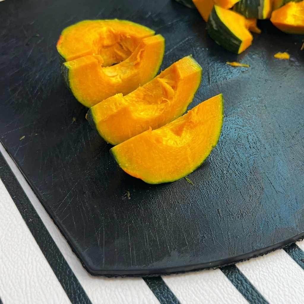 Pequeños trozos de calabaza de piel verde sobre una tabla de cortar negra.