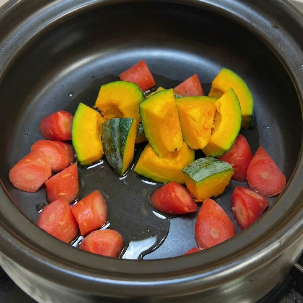 Una olla de barro negra con trozos de calabaza y zanahoria brillantes por el aceite antes de ser salteados.
