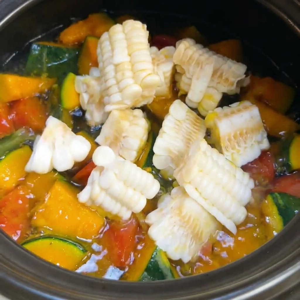 Segmentos de maíz fresco siendo añadidos a una olla con sopa de verduras burbujeante.
