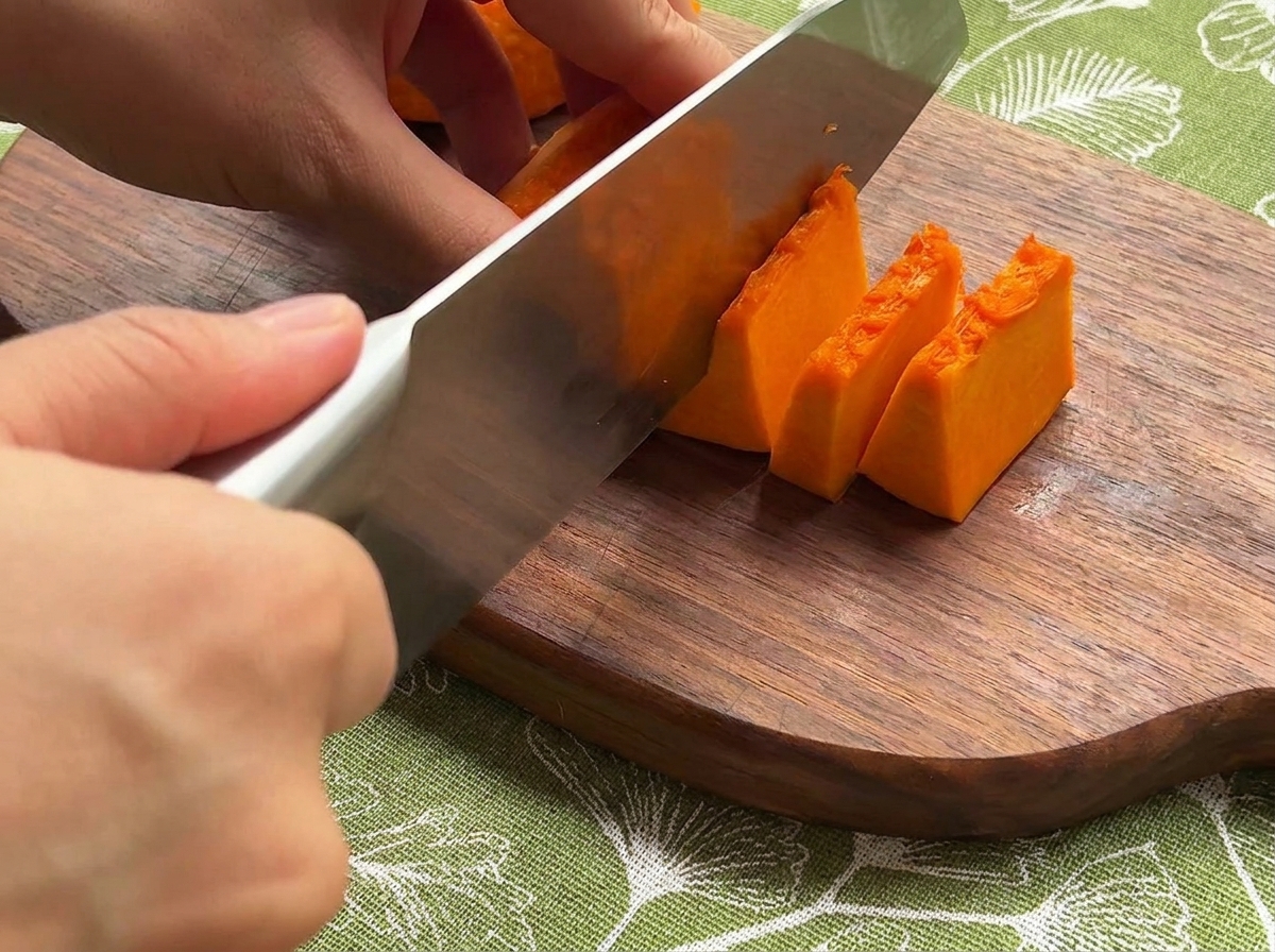 Calabaza, cebolla y zanahorias frescas siendo cortadas en trozos pequeños y uniformes sobre una tabla de madera.