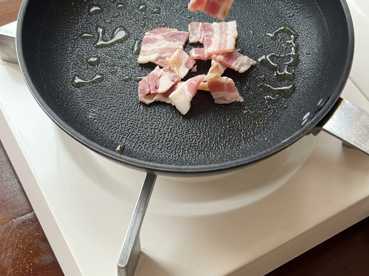 Tiras de tocino friéndose en una sartén hasta quedar doradas y crujientes.