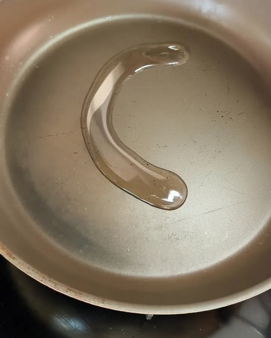 Rodajas finas de cebolla amarilla chisporroteando en una sartén con aceite de oliva caliente, mostrando un proceso de dorado ligero.