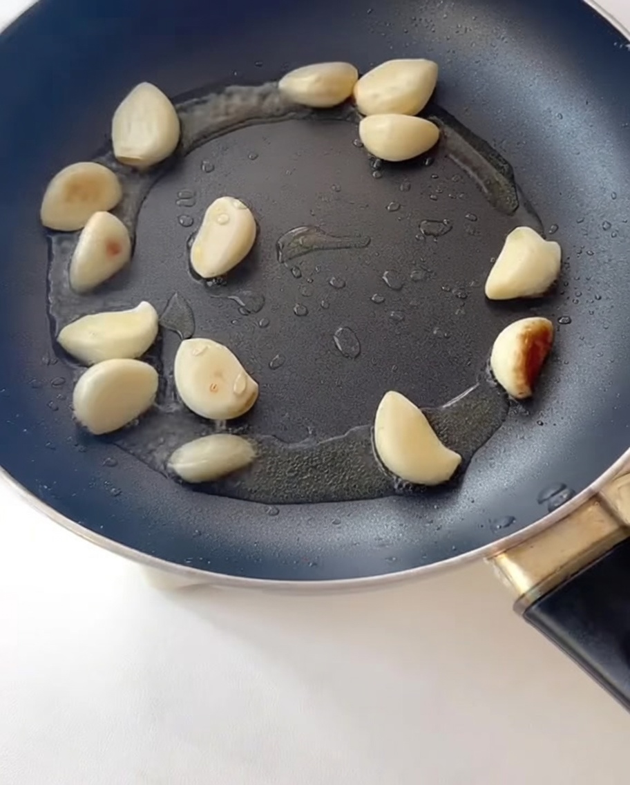 Tiras de tocino friéndose en una sartén junto al ajo salteado.