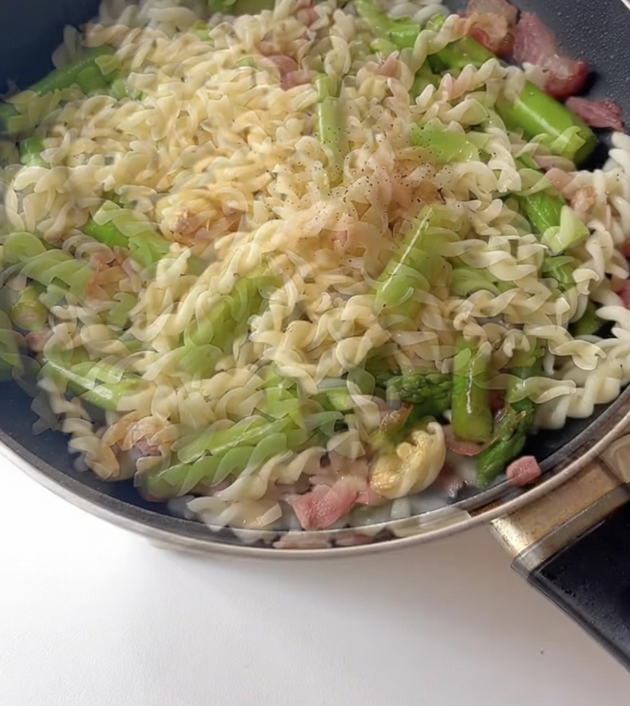 Condimentos, incluyendo pimienta negra, siendo espolvoreados sobre la pasta en la sartén.