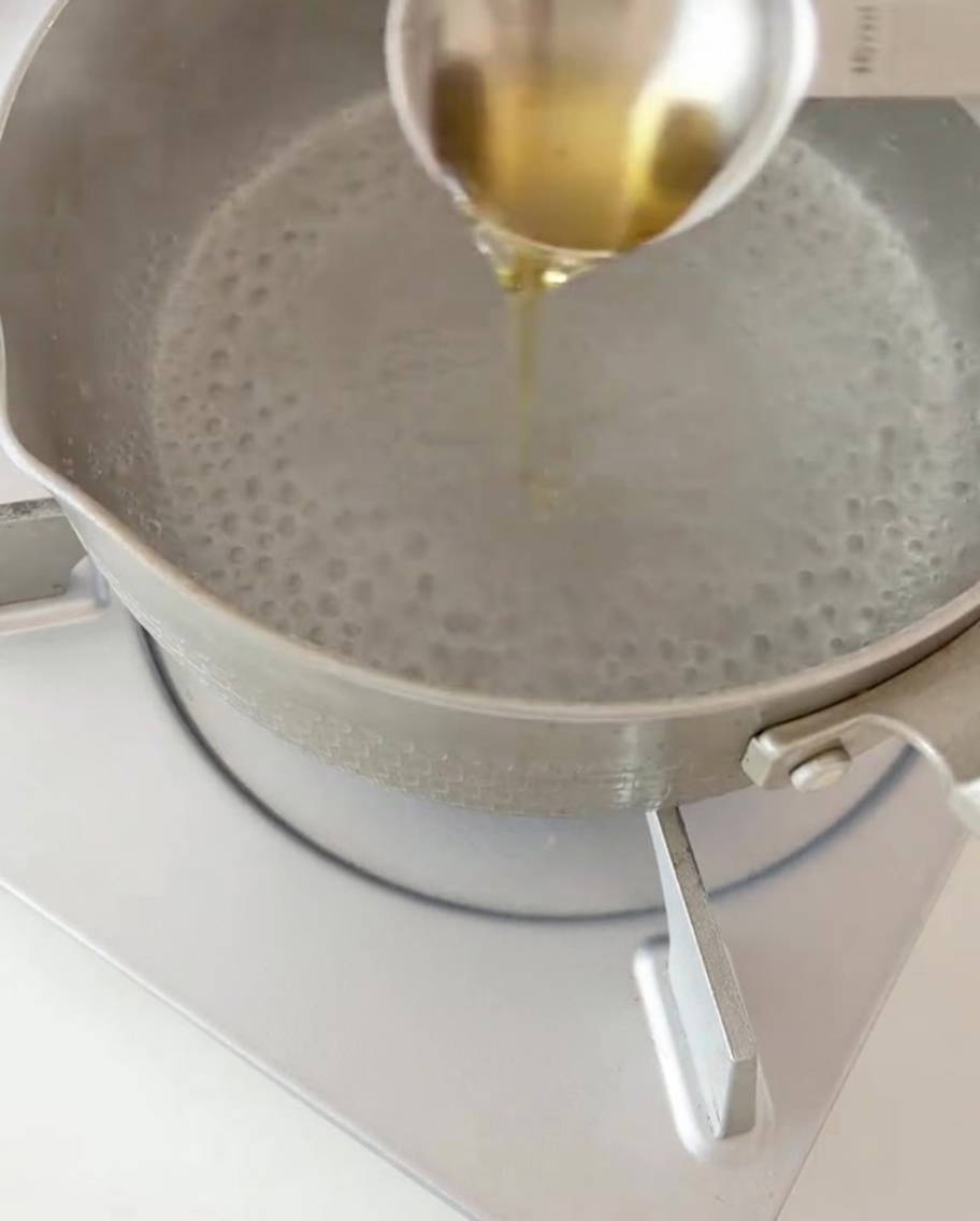 Pasta fusilli seca siendo añadida a una olla de agua hirviendo con un chorrito de aceite.