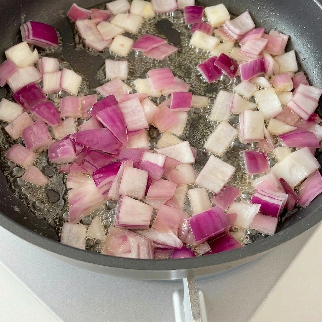 Trozos de tocino friéndose en una sartén con cebollas salteadas.