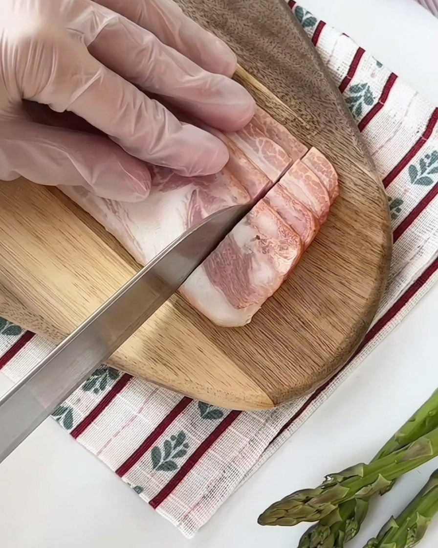 Tiras de tocino crudo cortadas en cuadrados pequeños y uniformes sobre una tabla de cortar de madera.