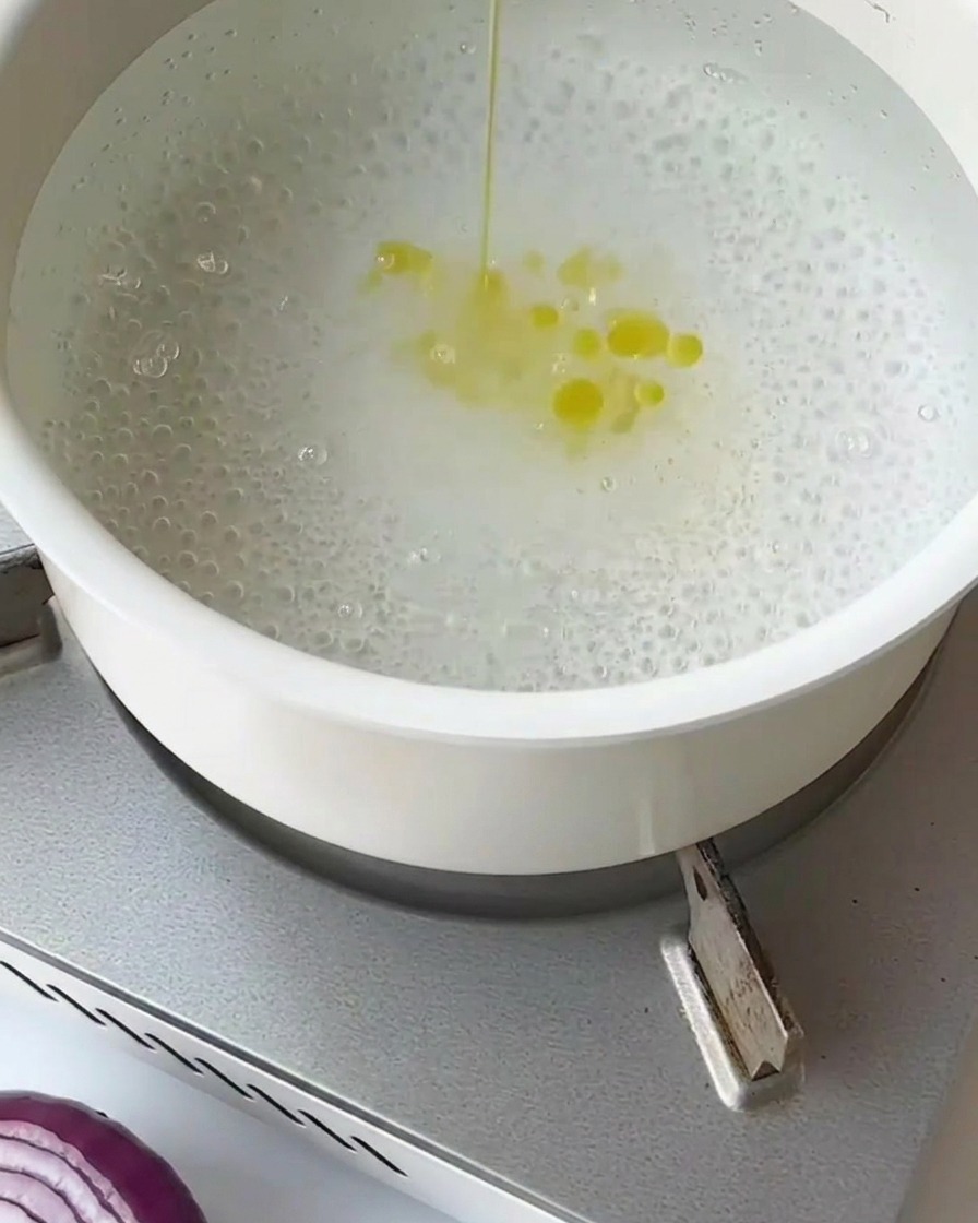 Segmentos de espárragos blanqueándose en agua hirviendo dentro de un colador de malla metálica.