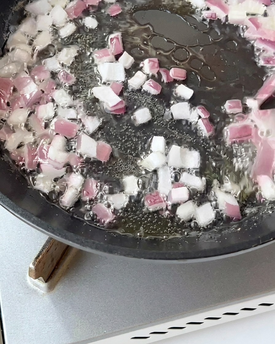 Trozos de tocino salteándose en una sartén con cebollas hasta quedar dorados.