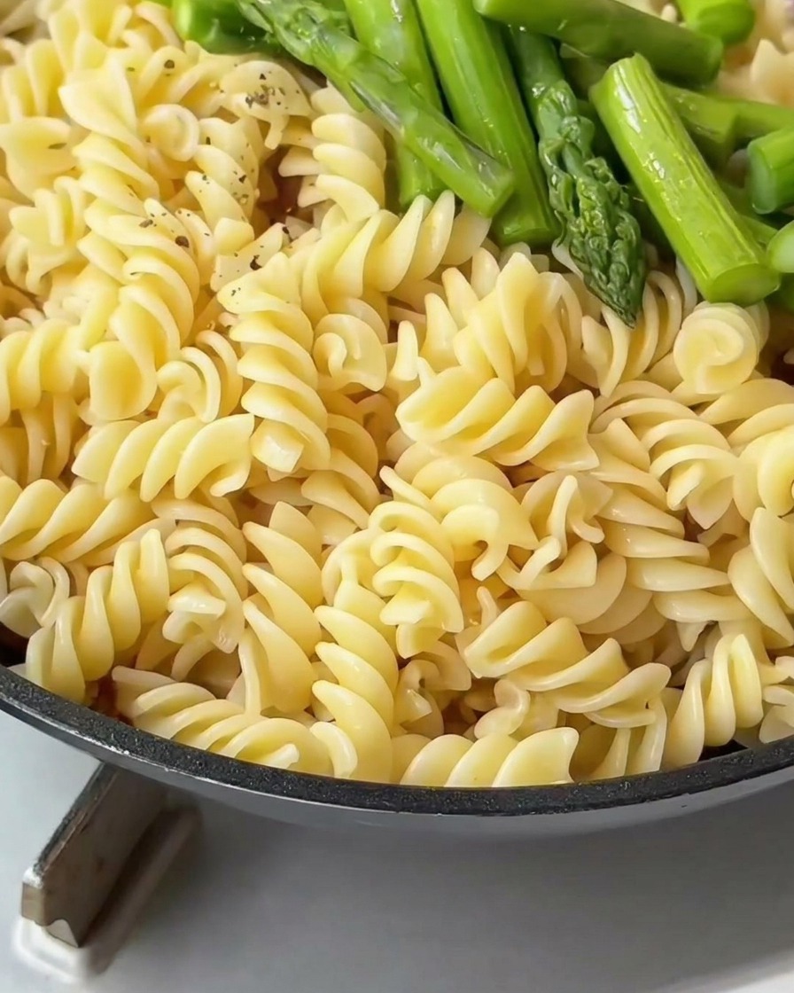 Pasta fusilli y espárragos verdes en una sartén siendo sazonados con pimienta negra recién molida.