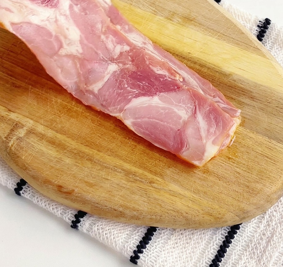 Tiras de tocino crudo siendo cortadas en trozos pequeños sobre una tabla de cortar de madera.