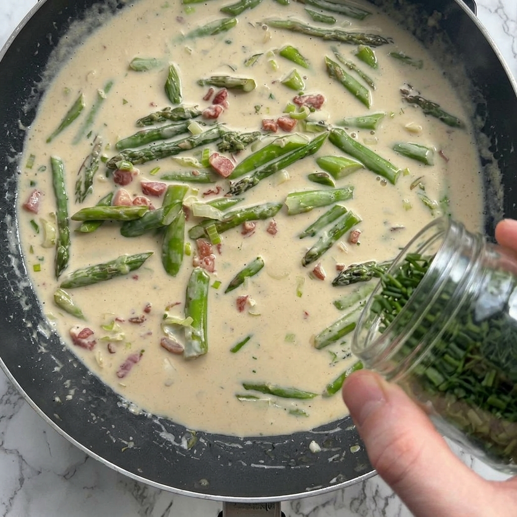 Queso parmesano y hierbas añadidas a la salsa cremosa en la sartén.