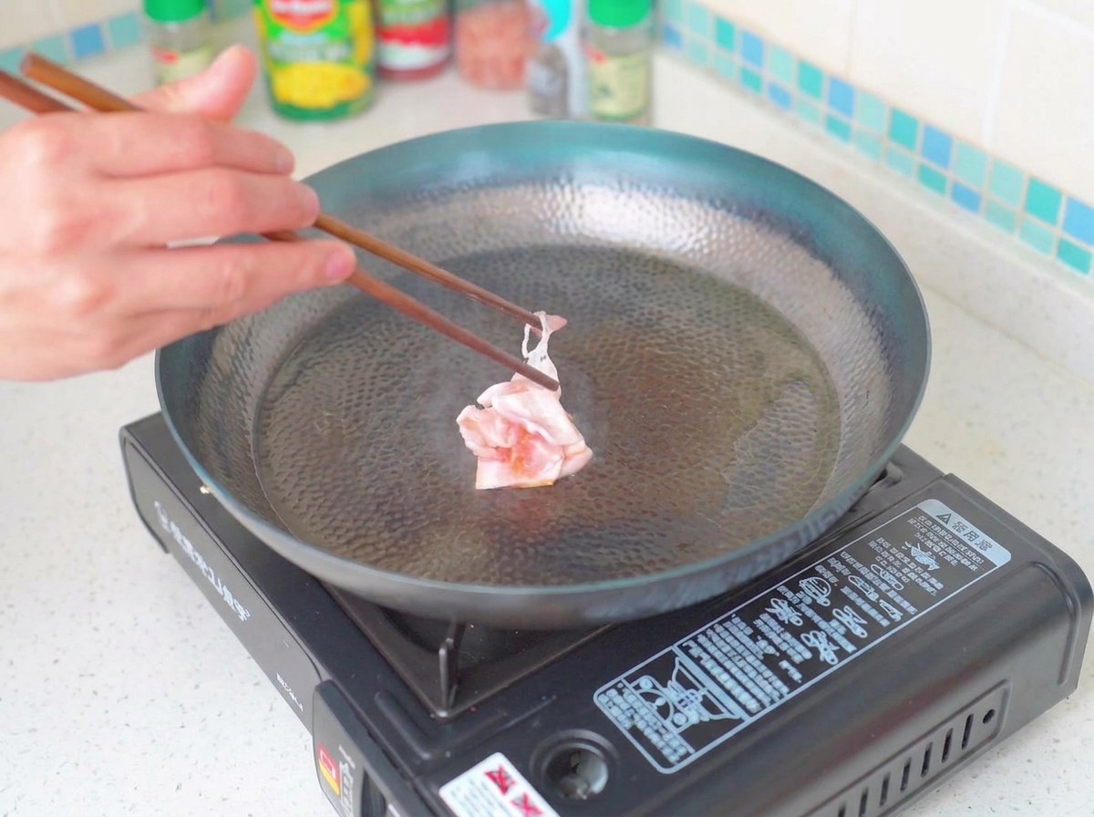 Trozos de tocino dorados y crujientes friéndose en una sartén.