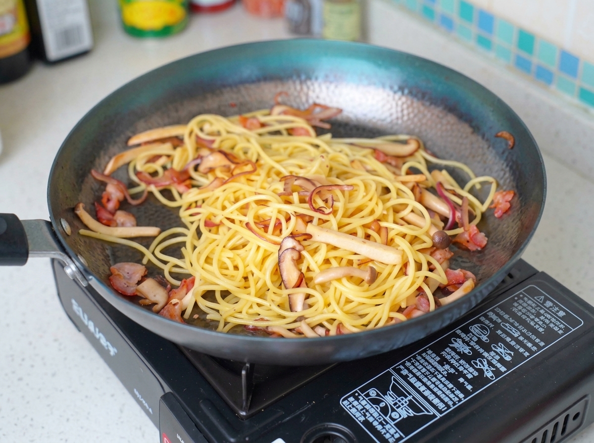 Leche vertiéndose sobre la mezcla de pasta, tocino y champiñones en una sartén.
