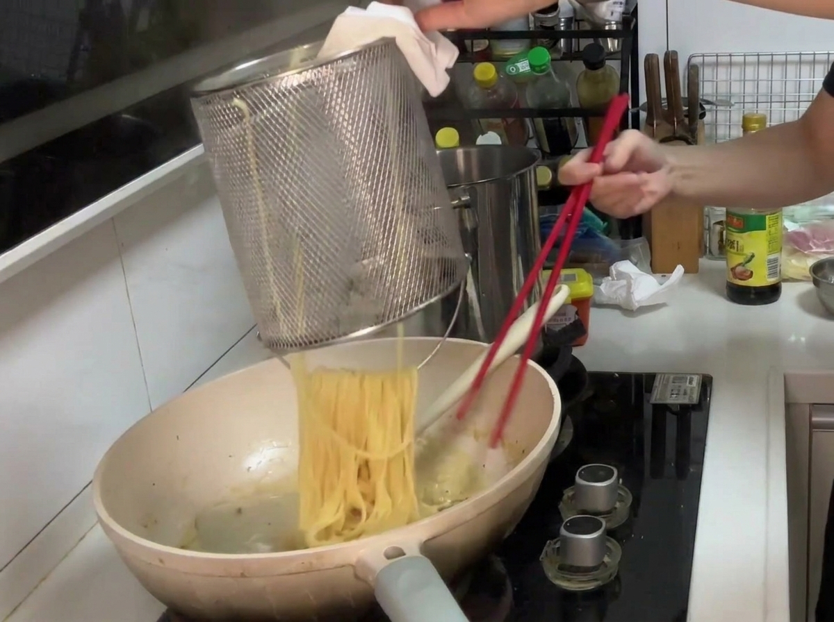 Pasta siendo añadida a la sartén con la salsa cremosa de champiñones.