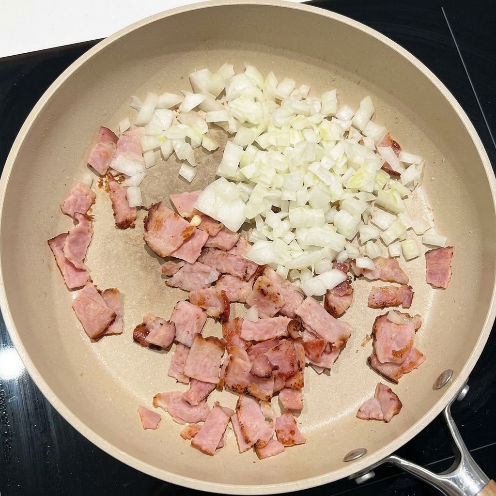 Cebolla blanca picada salteándose con trozos de tocino en una sartén grande.