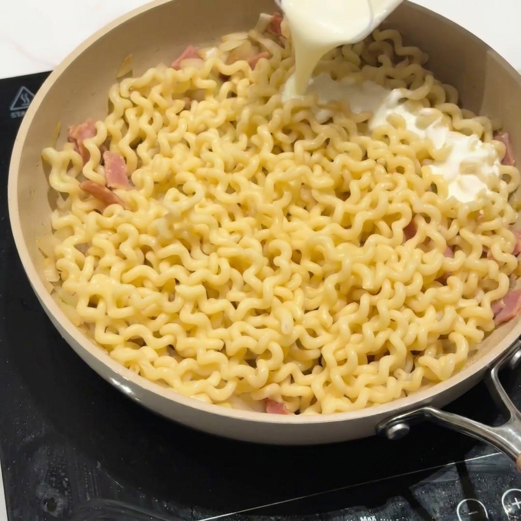 Leche baja en grasa vertiéndose sobre los fideos en una sartén para crear la salsa.