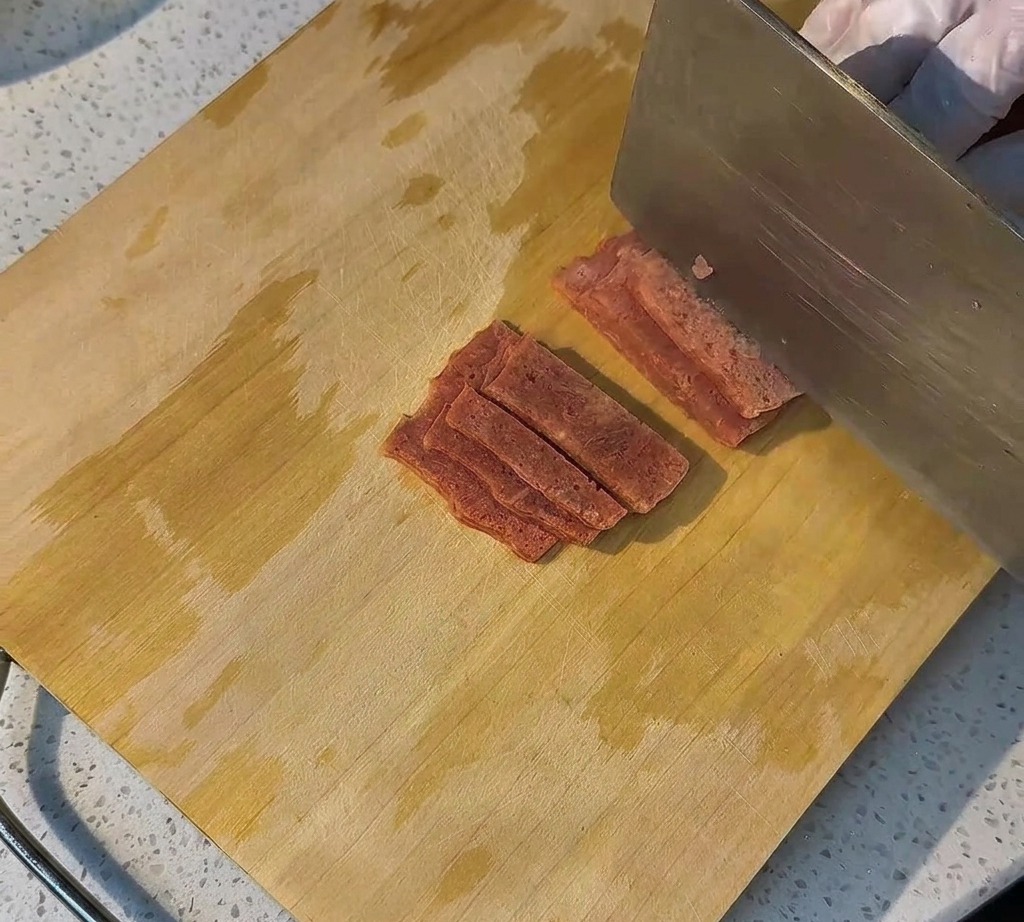 Rebanadas de tocino crudo dispuestas ordenadamente en una tabla de madera listas para cocinar.