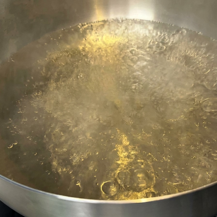 Una olla con agua hirviendo y una pequeña cantidad de aceite flotando en la superficie.