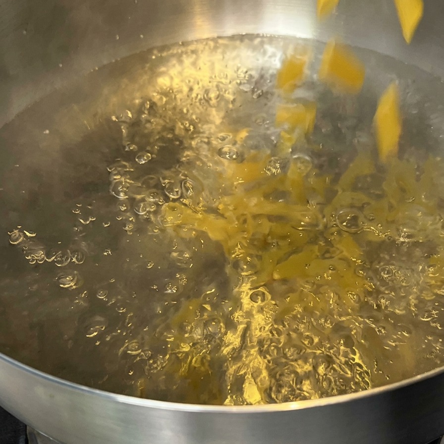 Pasta penne cayendo en una olla con agua hirviendo.