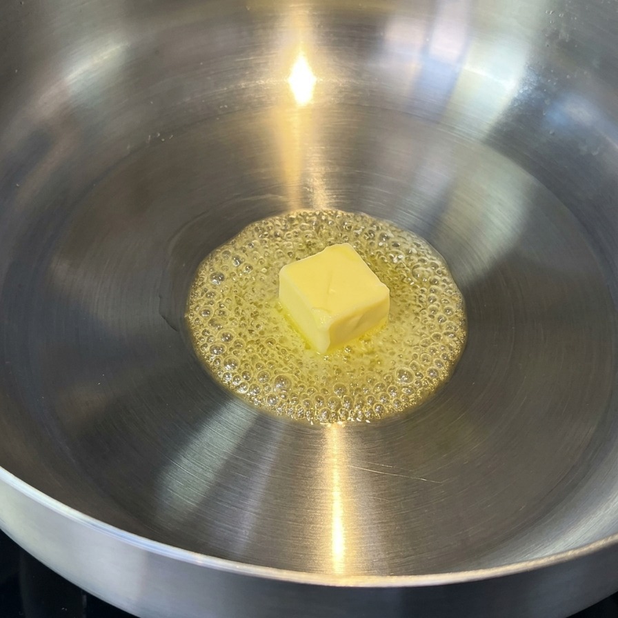 Mantequilla derritiéndose en una sartén de acero inoxidable, mostrando burbujas doradas.