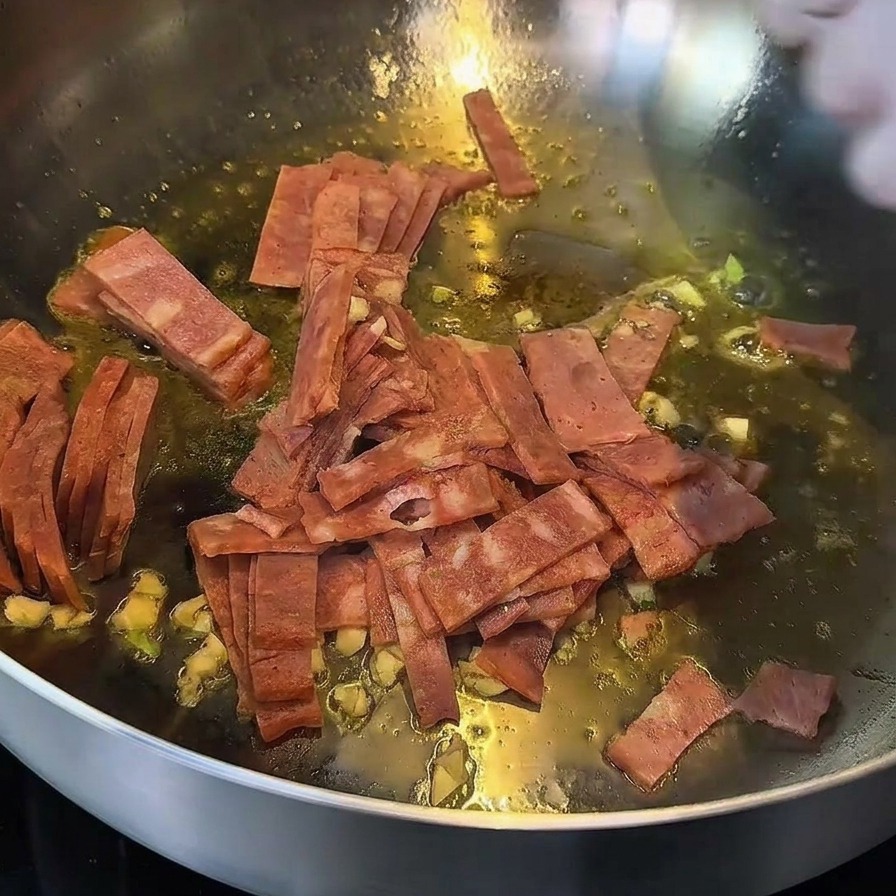 Tocino y ajo salteándose en una sartén, con los bordes del tocino dorados.