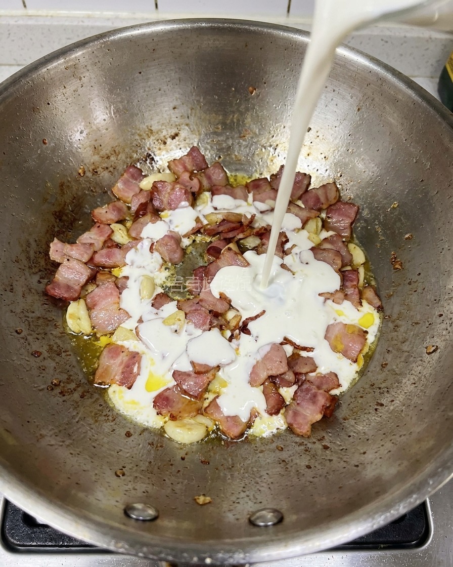 Crema espesa siendo vertida en una sartén que contiene trozos de tocino y ajo fritos.