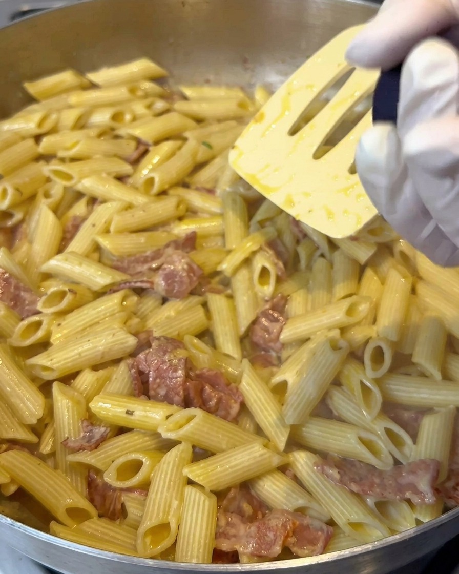 Sal de limón siendo molida sobre una sartén de pasta penne cremosa mientras se remueve.