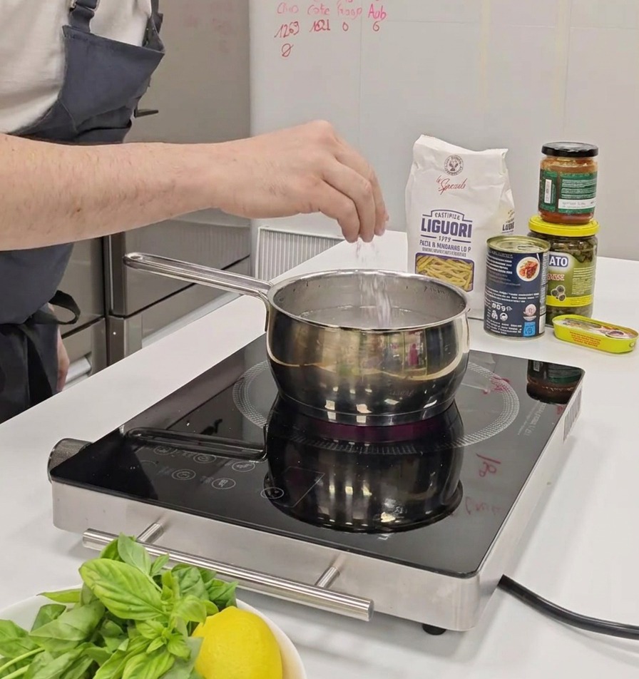 Una mano espolvoreando una pizca de sal en una olla de agua sobre una cocina de inducción.