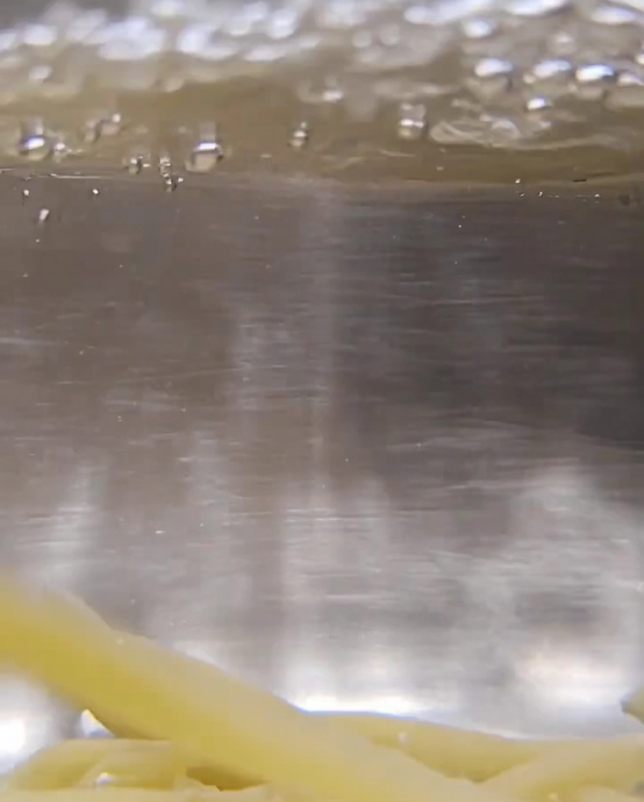 Primer plano de pasta trofie seca sumergida en agua hirviendo a borbotones.