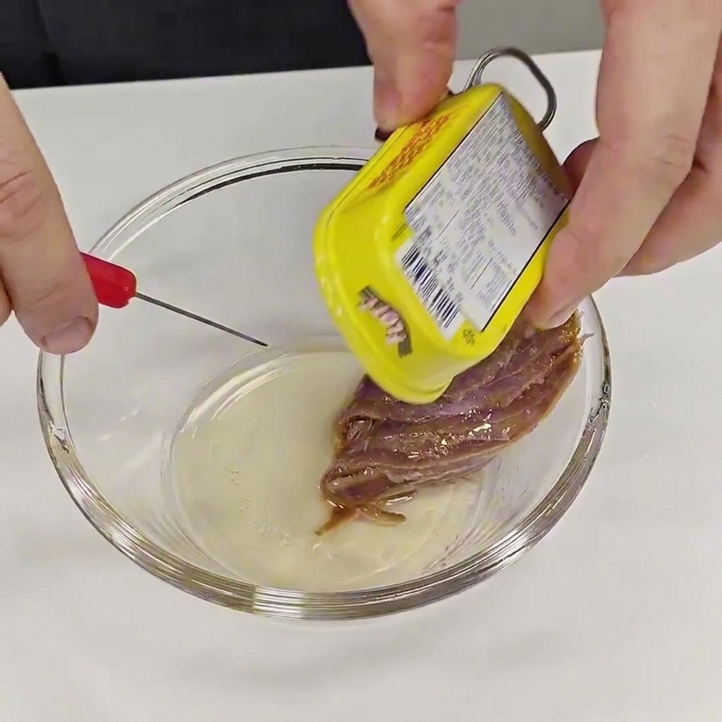 Unas manos sacando con cuidado un filete de anchoa de una lata amarilla para colocarlo en un pequeño bol de cristal.